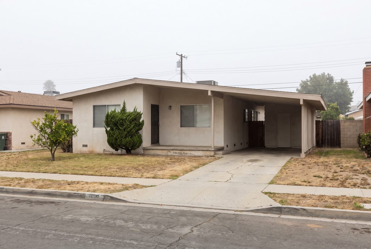 A single story postwar Los Angeles tract house with an attached carport, its stucco wall meeting the concrete at ground level with no foundation vents along the base.