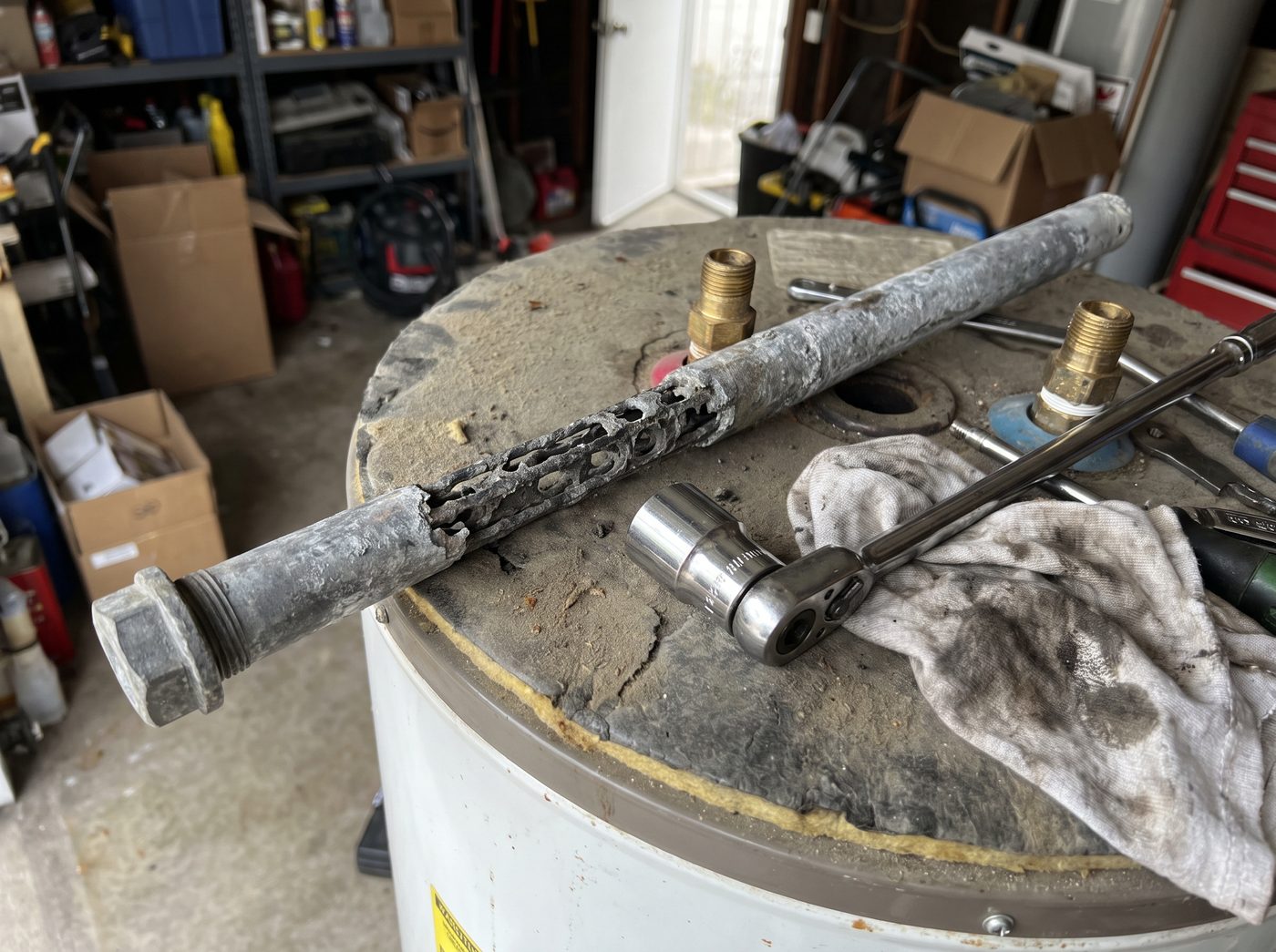 A spent magnesium anode rod eaten down to its steel core, lying on top of a water heater beside a socket and breaker bar.